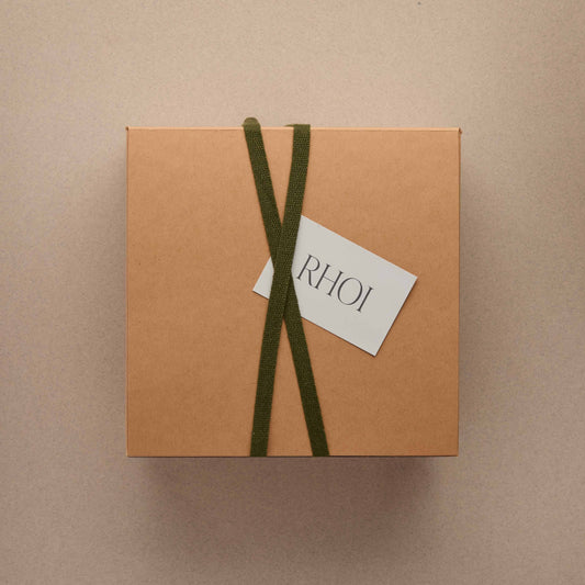 Brown gift box with green ribbon and 'RHOI' tag on a beige background