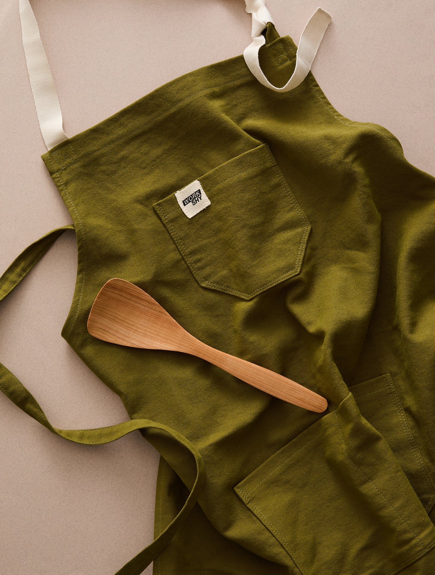 green cotton apron with wooden cooking spoon