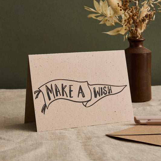Card with 'Make a Wish' design on a textured surface with a vase in the background