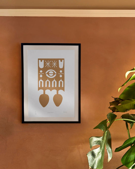 Framed artwork with welsh love spoon design on a orange wall with a plant in the foreground