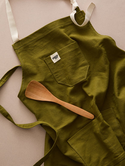 green cotton apron with wooden cooking spoon 